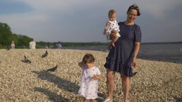 Ung mamma med sin bebis flicka döttrar utfodring svan och små ankungar fåglar bröd på en flod klädd i prickig klänning-familjens värderingar varm färg Sommarscen — Stockvideo