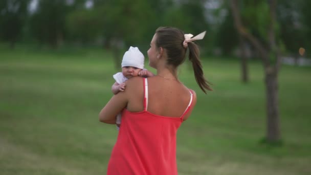 Jeune mère tenant et jouant avec son bébé garçon enfant dans le parc de la ville debout portant une robe rouge vif - Fils porte une casquette blanche - Valeurs familiales couleur chaude scène d'été portable — Video
