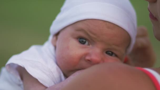 Giovane madre che tiene e gioca con il suo bambino neonato nel parco cittadino in piedi indossando un abito rosso brillante - Figlio indossa un cappuccio bianco - Valori familiari caldo colore scena estiva palmare — Video Stock