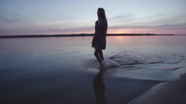 Kısa bir yaz elbise yürüyüş genç kadın yürüyüş ve gün batımında yaşam ve doğa uzak arka plan zevk plaj boyunca sıçrayan