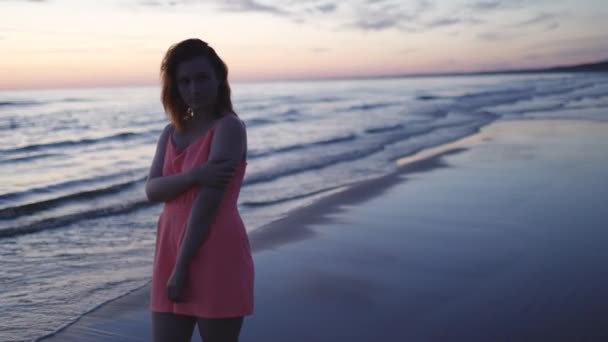 Jovem mulher em brilhante terno vestido vermelho de pé sobre a água desfrutando de vida e natureza longe fundo no pôr do sol — Vídeo de Stock