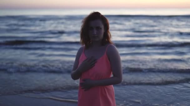 Mladá žena v jasně jemných červených šatech stojící na vodě těší život a příroda daleko na pozadí při západu slunce — Stock video