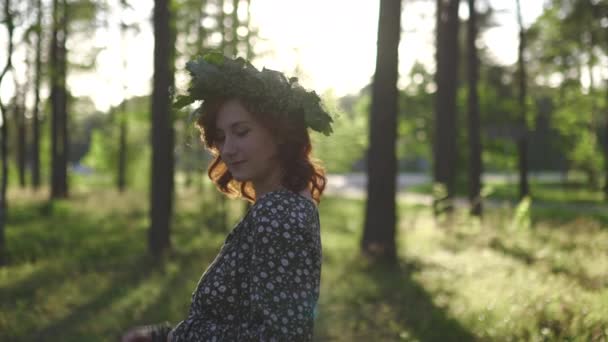 Walking: Redhead ung kvinna i en krans under traditionell lettiska Ligo midsommar dag-kaukasiska vit flicka klädd i en prickig sommarklänning med ett bälte i solig solnedgång — Stockvideo