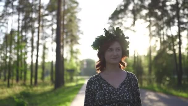 Wandelen: Redhead jonge vrouw in een krans tijdens de traditionele Letse Ligo Midzomerdag-blanke wit meisje dragen een gestippelde zomer jurk met een riem in zonnige zonsondergang — Stockvideo