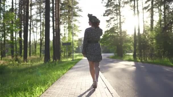 Gångavstånd: rödhårig ung kvinna i en krans under traditionell lettisk Ligo midsommar dag-kaukasisk vit flicka klädd i en prickig sommarklänning med ett bälte i solig solnedgång — Stockvideo