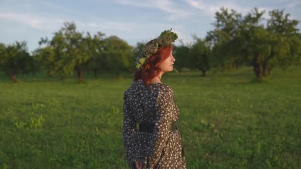 Redhead ung kvinna i en krans under traditionella lettiska Ligo midsommar dag-kaukasiska vit flicka klädd i en prickig sommarklänning med ett bälte i solig solnedgång — Stockvideo