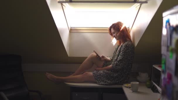 Mensajes de texto: Mujer pelirroja sonriente positiva usando el teléfono de tecnología - Chica blanca caucásica con un vestido de verano punteado en un ático — Vídeos de Stock