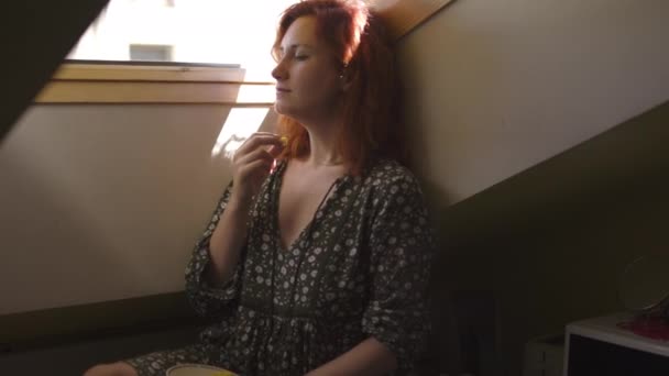 Positieve lachende redhead vrouw eten Ligo Cheese-Kaukasische wit meisje dragen een gestippelde zomer jurk op een zolder — Stockvideo