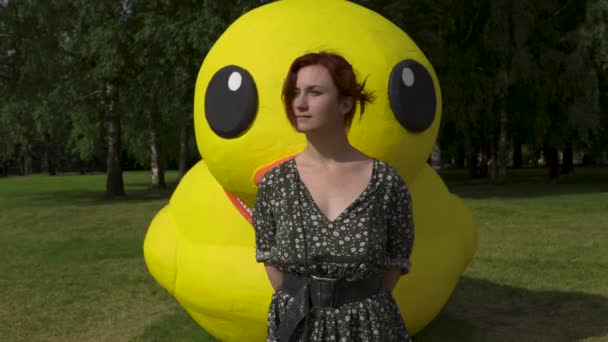 Frente: Mujer pelirroja y un enorme pato amarillo artificial no real o vivo - niña blanca caucásica con un vestido de verano punteado — Vídeos de Stock