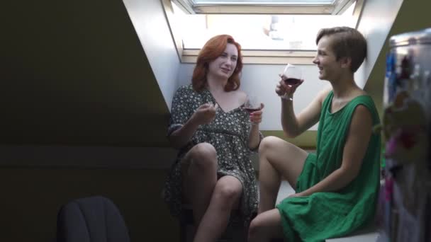 Zwei Frauen plaudern und trinken Rotwein aus großen Gläsern - kaukasische weiße Mädchen lachen in einem gepunkteten Sommerkleid und einem grün schlichten — Stockvideo