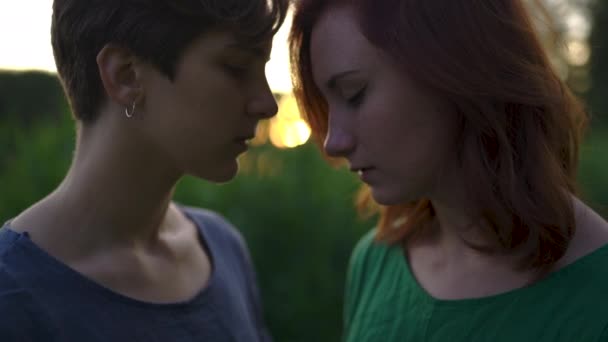 Dos mujeres serias con los ojos cerrados disfrutando de la puesta de sol frente a la hierba alta casi besándose con los labios cerca el uno del otro — Vídeos de Stock