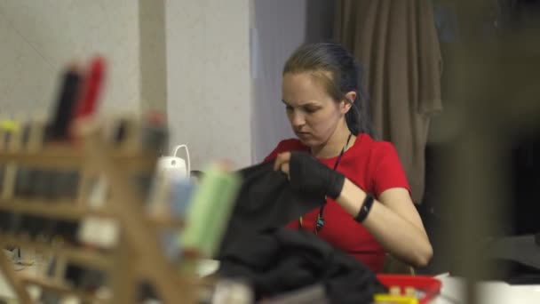 网络朋克时装设计师在她的工作室缝纫使用机器 - 白种白人妇女穿着红色T恤和黑色手套与剪刀挂在她的胸部 — 图库视频影像
