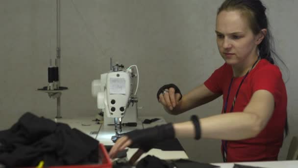 Cyber punk modedesigner på jobbet i sin Studio sömnad med maskin-kaukasiska vit kvinna klädd i röd t-shirt och svarta handskar med sax hängande över bröstet — Stockvideo
