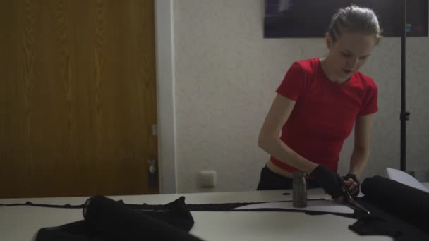 Diseñadora de moda cyber punk en el trabajo en su patrón de corte de estudio - Mujer blanca caucásica con camiseta roja y guantes negros con tijeras colgando sobre su pecho — Vídeos de Stock