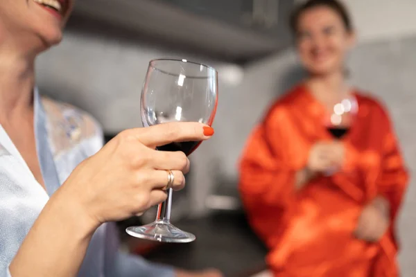 Mutfakta sohbet eden ve camdan kırmızı şarap içen iki kadın - Biri mavi sabah elbisesi, diğer kırmızı bornoz elbisesi - Gülerek ve gülümseyerek