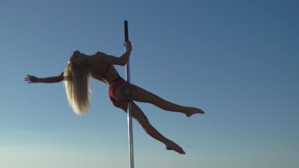 Flexibilní ženská tanečnice v červeném sportovním prádle nosí na pylonu při západu slunce na pláži-dračí tetování a akrobatickou gymnastiku. — Stock video