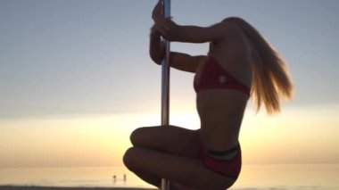 Yakın kırmızı spor iç çamaşırı Esnek kadın kutup dansçısı bir plajda gün batımında pilon üzerinde egzersiz giymek - Ejderha dövme ve Akrobatik jimnastik