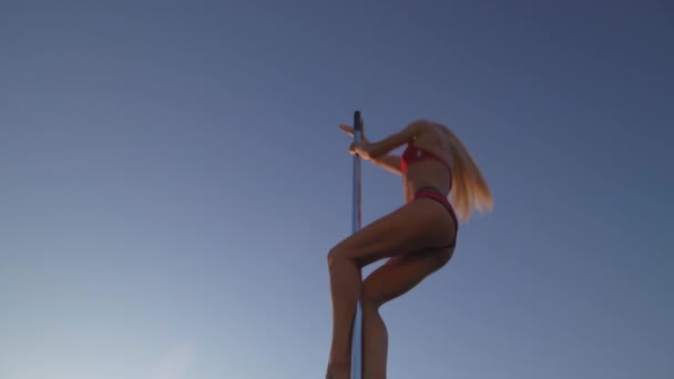 Flexibilní ženská tanečnice v červeném sportovním prádle nosí na pylonu při západu slunce na pláži-dračí tetování a akrobatickou gymnastiku. — Stock video