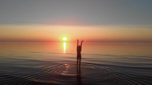 Levantamiento de manos aéreas: silueta de mujer caminando hacia la puesta del sol sol en el mar — Vídeos de Stock