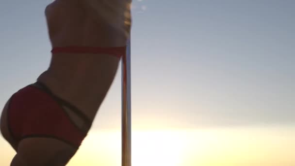 Nahaufnahme einer flexiblen Polentänzerin in roter Sportunterwäsche, die bei Sonnenuntergang am Strand auf dem Pylon turnt - Drachen-Tätowierung und akrobatische Gymnastik — Stockvideo
