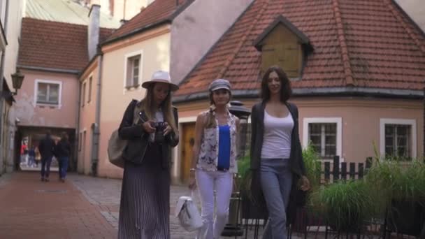 Tre resande tjej vänner med lätta ryggsäckar kontrollera bilder på DSLR kamera och utforska Riga City-Travel turism koncept efter överföring från flygplats-bär hattar och jeans — Stockvideo