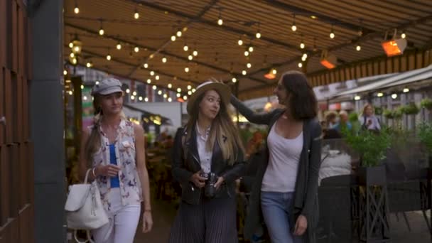 白い帽子を取る - リガ市を探索する軽いバックパックを持つ3人の旅行の女の子の友人 - 空港からの転送後の旅行観光の概念 - 帽子とジーンズを着用 — ストック動画