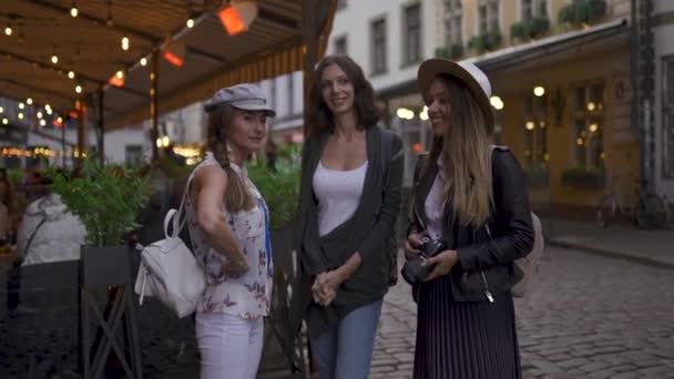 Chatting and laughing Three traveling girl friends with light backpacks exploring Riga city - Travel tourism concept after transfer from airport - Wearing hats and jeans — Stock Video