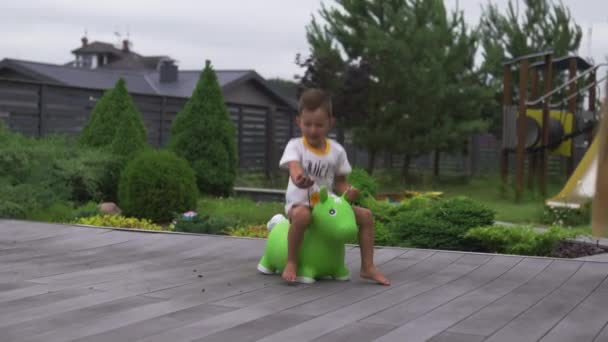 Baby jongen zoon kind springen paardrijden groene speelgoed paard in een groene tuin-familie waarden warme kleur zomer scène — Stockvideo