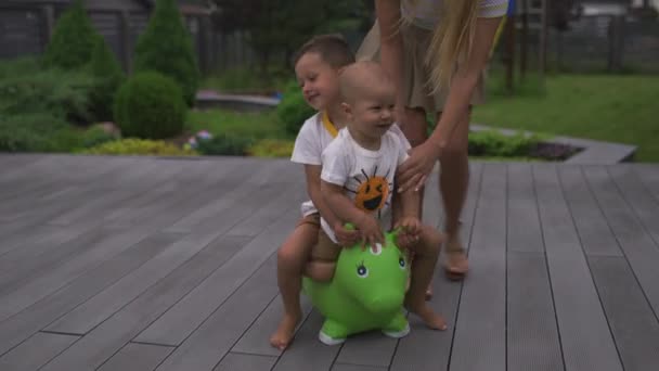 Baby jongen zoon kind springen paardrijden groene speelgoed paard in een groene tuin-familie waarden warme kleur zomer scène — Stockvideo