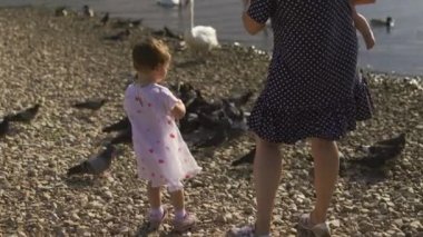Genç anne onun bebek kız kızları ile beslenen kuğu ve küçük ördek yavruları bir nehir de noktalı elbise giyen ekmek - Aile değerleri sıcak renk yaz sahnesi