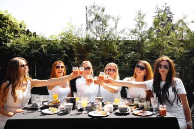 Group of friends in white having breakfast in garden at table with food and communicating, laughting concept