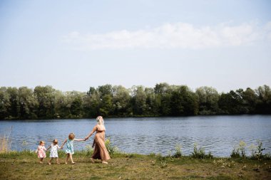 Anne karahindiba üfleme bir parkta onun bebek kız ile kaliteli komik oyun zamanı olan - Genç sarışın hippi - Kızları çilek baskı ile benzer elbiseler giymek - Aile değerleri