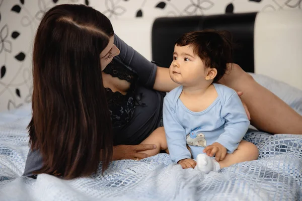 Madre embarazada acostada con su hijo bebé en la cama del dormitorio jugando y divirtiéndose - Niño asiático de etnia mixta con camisa de cuerpo azul con dibujos animados oso sonriente — Foto de Stock