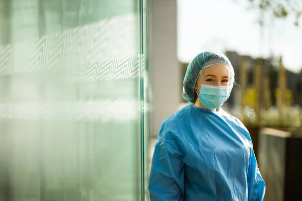 Médico o enfermera en máscara quirúrgica y gorra quirúrgica mirándote — Foto de Stock