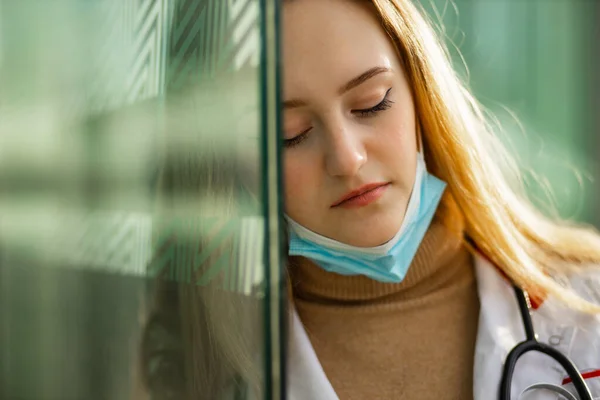 Vista cercana de la triste doctora o enfermera vestida con bata médica blanca quitándose la máscara quirúrgica — Foto de Stock