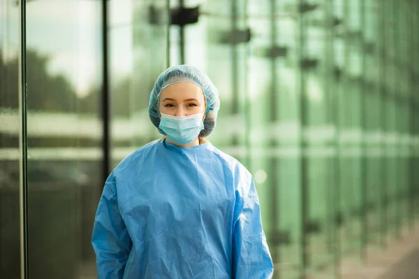Médico de atención médica médico o enfermera en máscara quirúrgica y gorra quirúrgica mirándolo — Foto de Stock