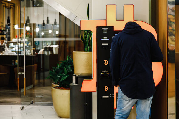 Bald man uses Bitcoin ATM machine in mall for cryptocurrency exchange