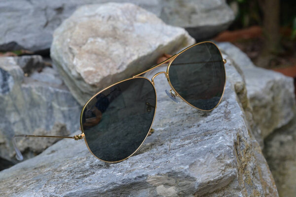 Gold frame aviator black sunglasses on rock