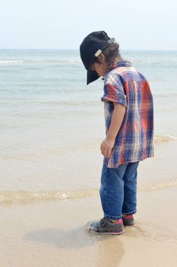 Güneşli bir günde sahilde denizde duran çocuk.