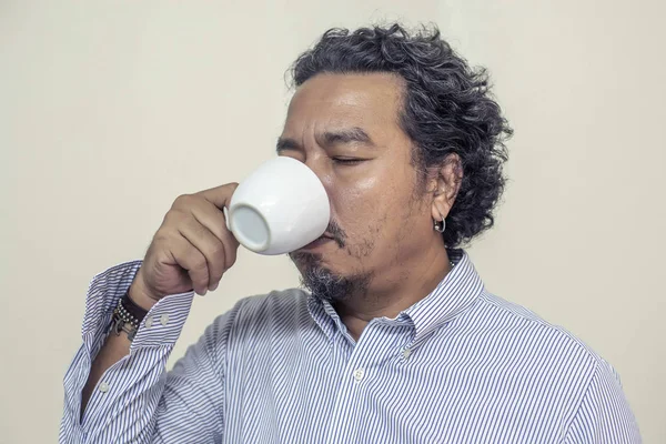 Чоловік п'є каву в чашці, посміхається і щасливий — стокове фото