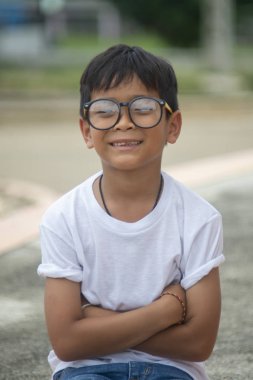 Asyalı çocuk gözlüklü beyaz bir t-shirt giyiyor, oturan, mutlu gülümseyen