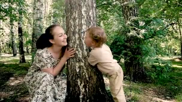 Young beautiful mother plays with her 2 year old cute son by the tree. — Stock Video