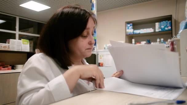 Pharmacienne femme 40-50 ans regarde la liste des médicaments sur papier à la pharmacie. Un chirurgien spécialiste dans une clinique examine une ordonnance. Pharmacie vendant des médicaments . — Video