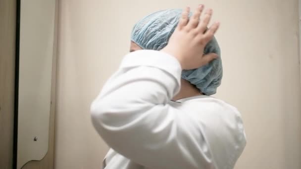 Medico donna 40-50 anni indossa una maschera medica e cappello. Lunga giornata di lavoro nel concetto di strutture mediche. Un duro lavoro. Il lavoro di un'infermiera. Il chirurgo si prepara per l'intervento — Video Stock