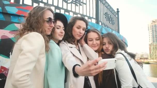 Selfies al aire libre en la ciudad. Cinco chicas tomando fotos en un smartphone sobre un fondo de graffiti. jóvenes. concepto de turismo. Feliz Summer Fun. 20-25 — Vídeo de stock