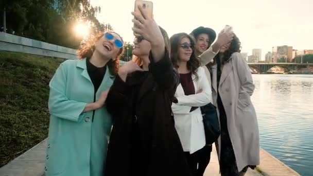 Selfies al aire libre en la ciudad. Cinco niñas tomando fotos en un teléfono inteligente en un fondo del parque. jóvenes. concepto de turismo. Feliz verano divertido — Vídeo de stock