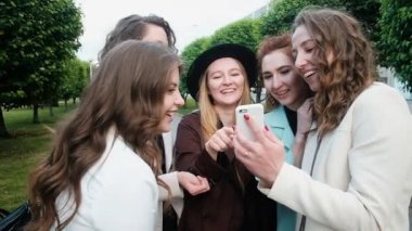 Bir grup güzel kız internetteki akıllı telefon fotoğraflarına bakıyor. Genç insanlar. Turizm konsepti. Mutlu yazlar. Eğlenceliydi. 20-25 yıl.