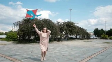 Genç ve güzel bir kadın renkli bir uçurtmayla koşuyor. 20-25 yaşlarında. Kız şehirde kaygısız yürüyor. Hafta sonu Tatili Konsepti