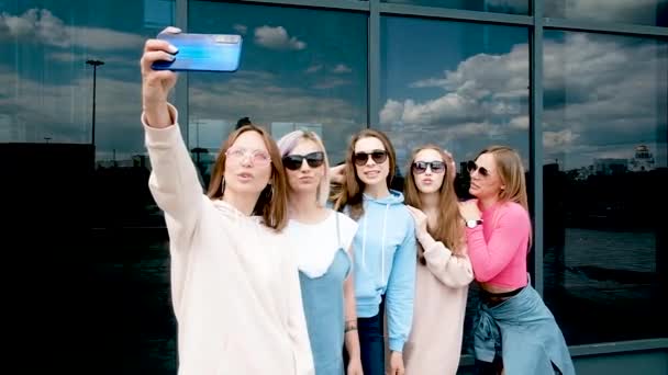 Belle ragazze che si fanno un selfie all'aperto in città. Cinque ragazze su uno smartphone vicino a finestre di vetro. Gioventù, gioventù. camminare in primavera. 20-25 anni — Video Stock