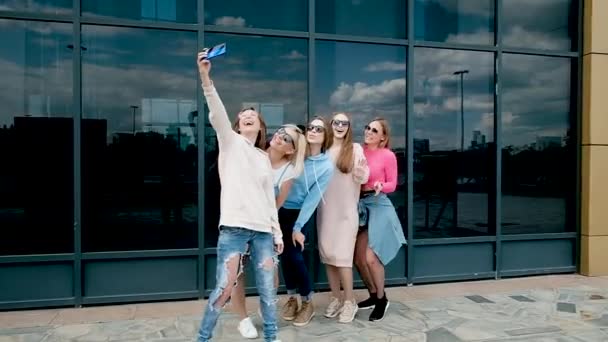 Hermosas chicas tomando una selfie al aire libre en la ciudad. Cinco novias en un smartphone cerca de ventanas de cristal. juventud, juventud. caminar en primavera. 20-25 años — Vídeo de stock